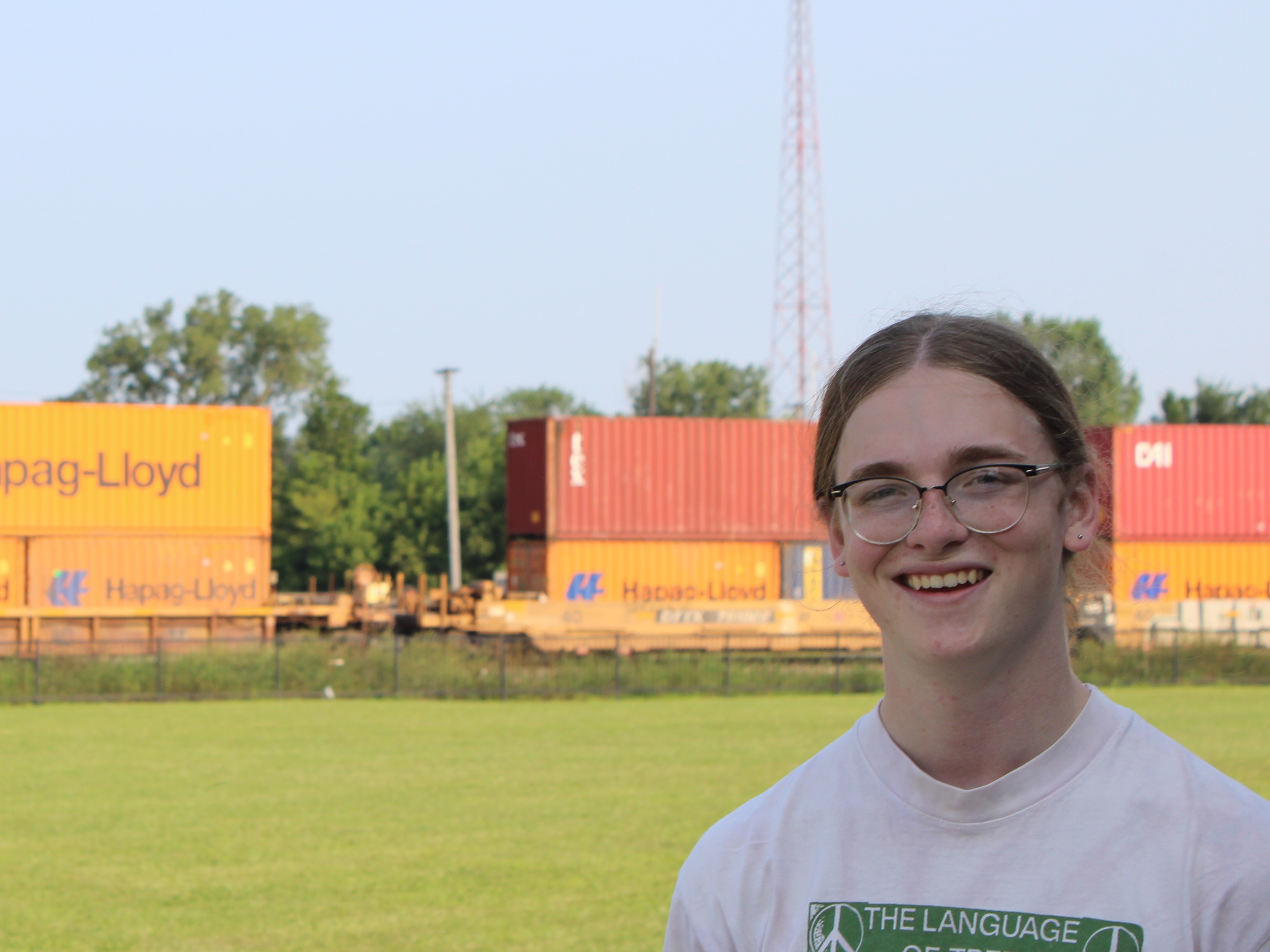 A person with glasses smiling in front of a freight train