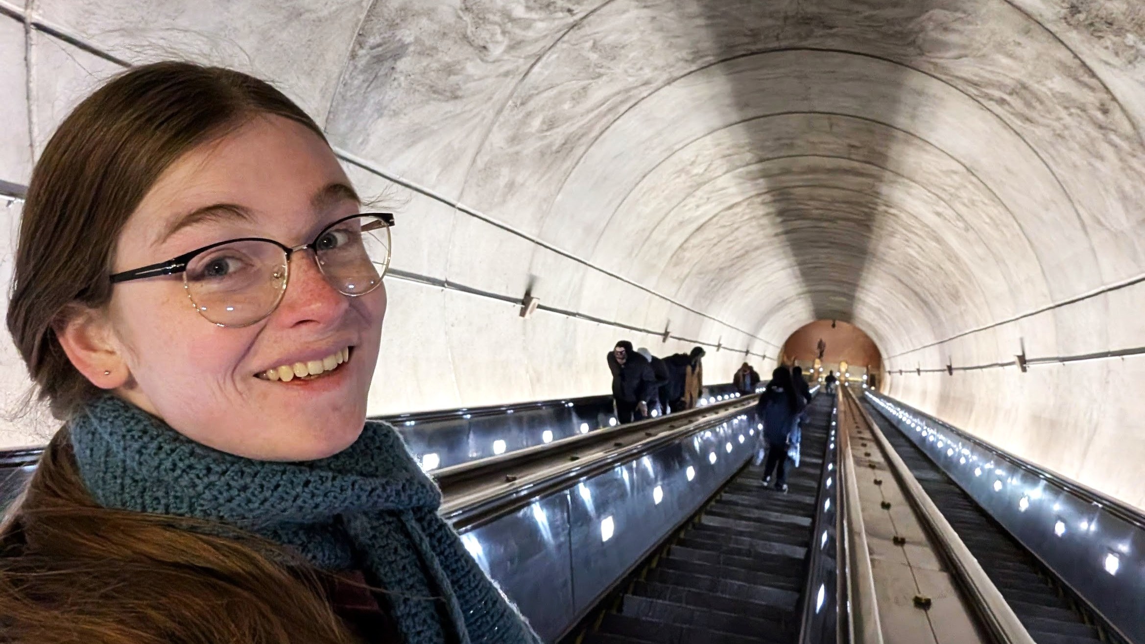 A person with glasses smiling on an escalator