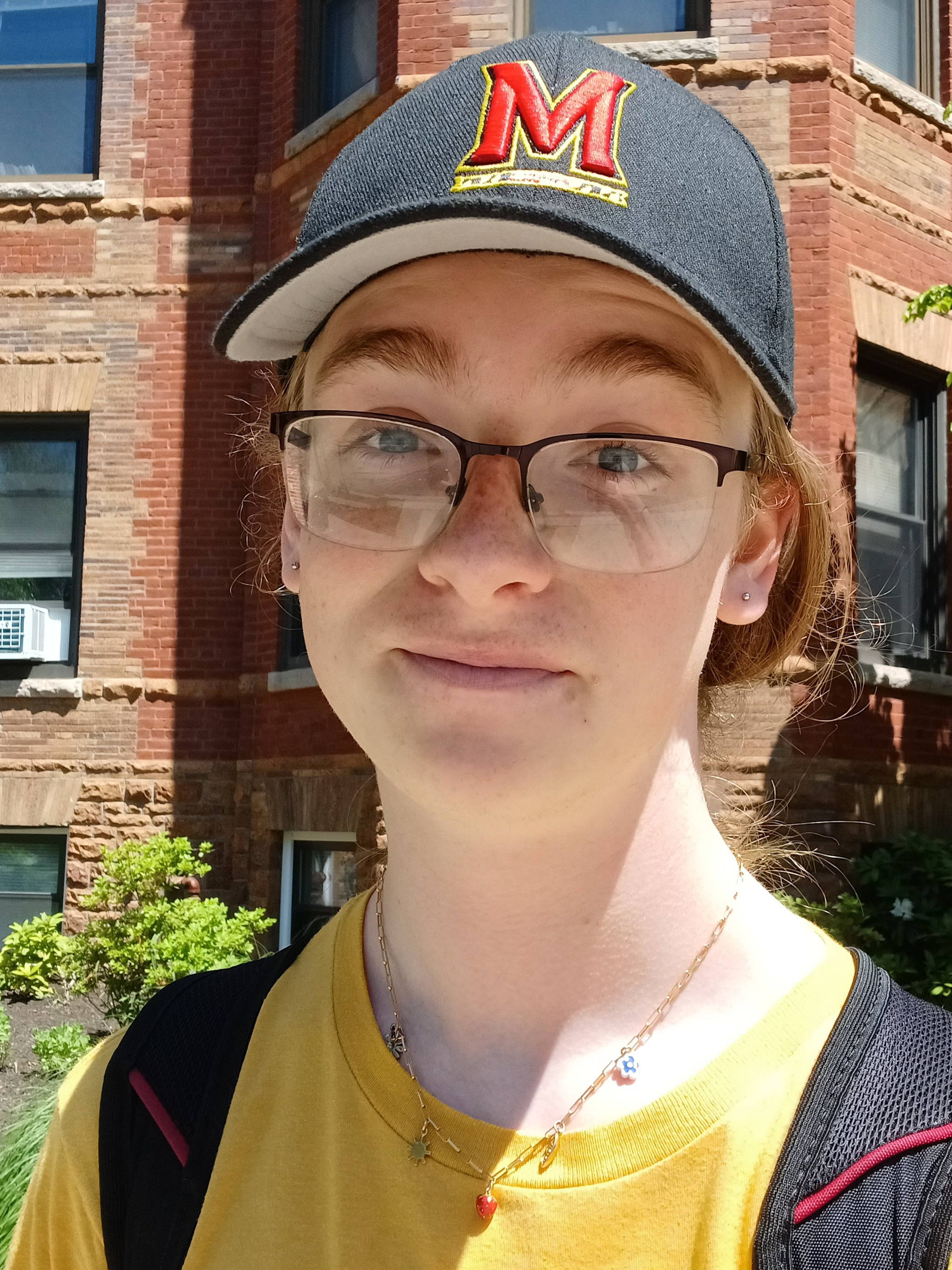 A person with a hat and necklace smiling in front of a building